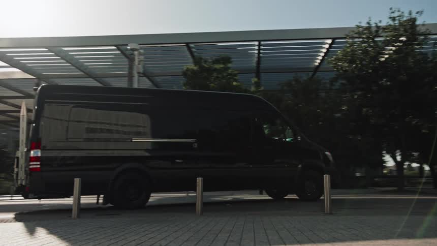 A large black transport van with tinted windows travels past an office building entrance