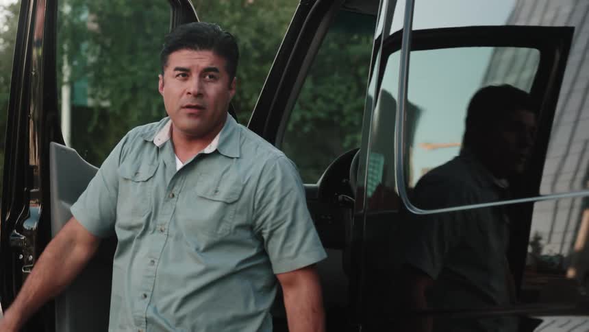 Focused male worker exists a large van, closes the driver's door and walks toward the rear