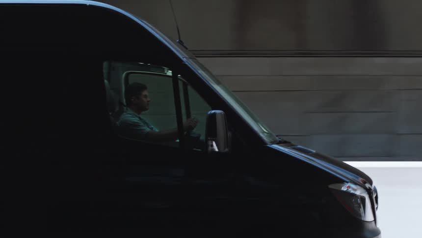A focused working man navigates a black transport van along the highway