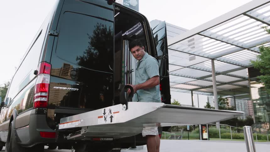 A man lowering a ramp on the back of a black van in a city setting