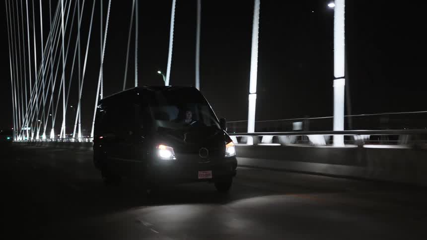 A dark van driving over a suspension bridge at night