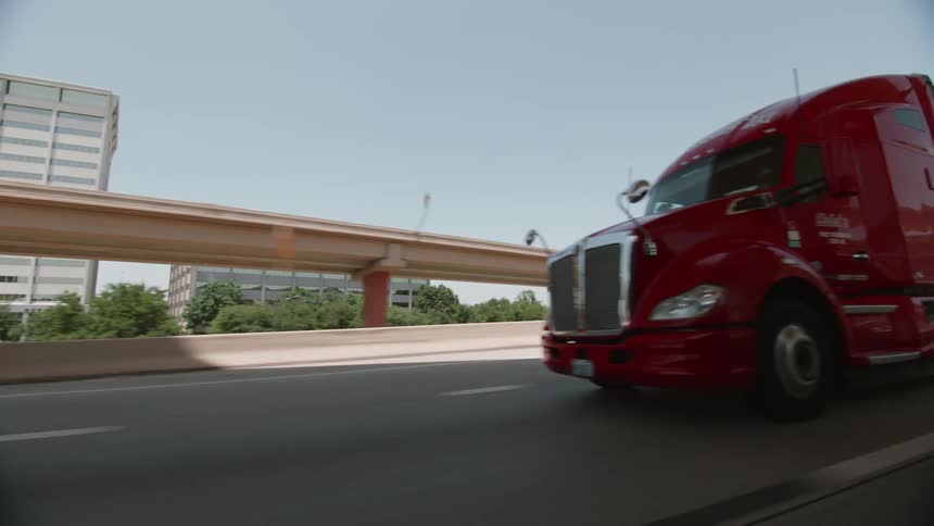 A red semi truck driving on an urban highway in the daytime