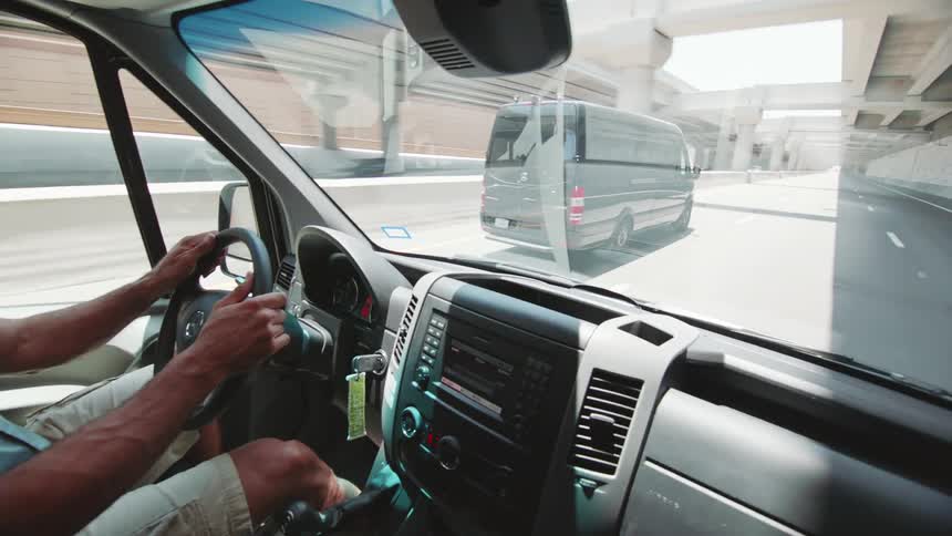A man smiles and waves at a passing van as they both drive on a sunny highway