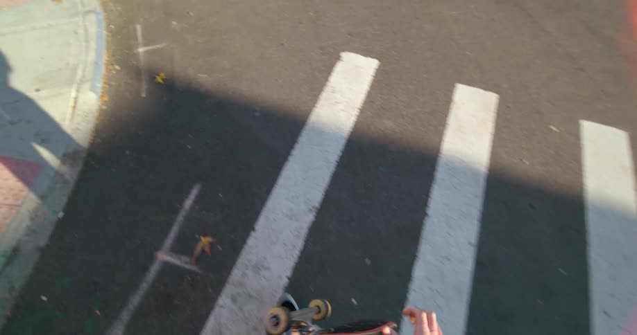 Skateboarder carries skateboard along crosswalk as sun casts shadow