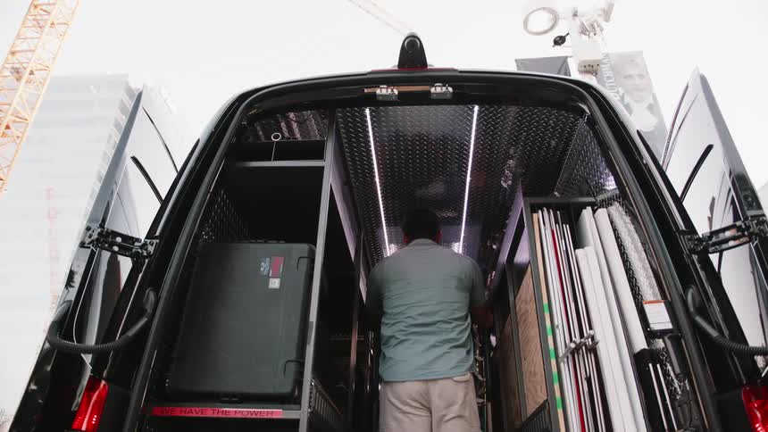 Happy worker prepares to unload equipment from the cargo section of a black transport van using a dolly cart