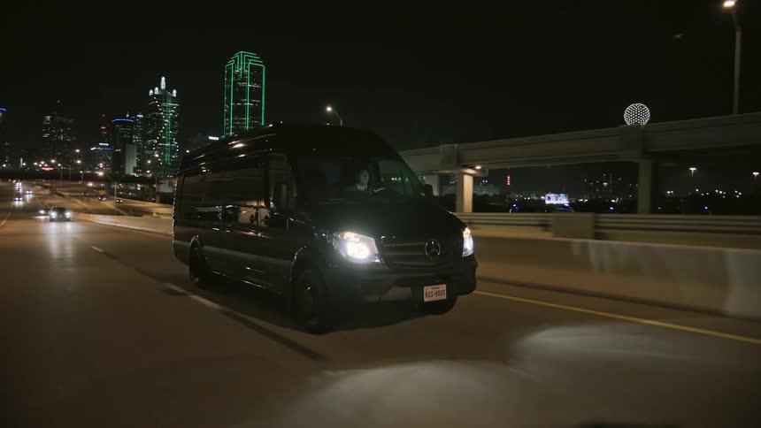 A man drives a large black van on a city highway at night