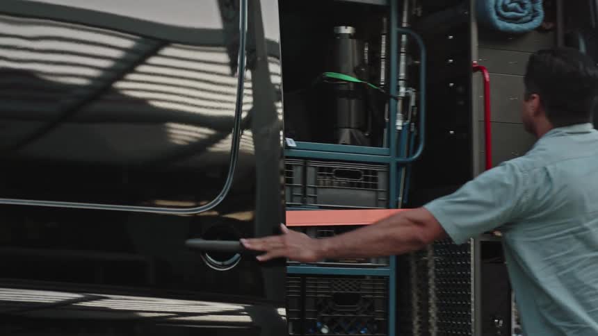 Happy male worker opens the sliding door on a black transport van, revealing plastic crates full of equipment and supplies