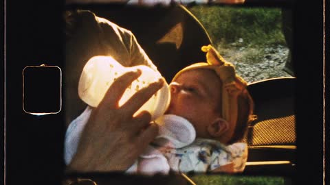 Mother feeding her baby daughter on the seat of a car parked near a field at sunset