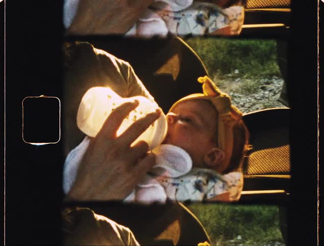 Mother feeding her baby daughter on the seat of a car parked near a field at sunset
