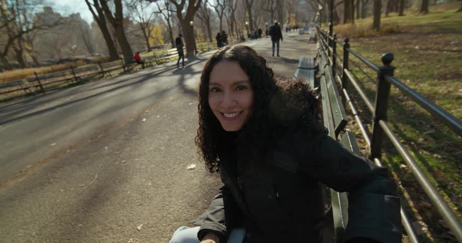 A woman sits on a park bench and holds a mans hand and rubs it as people walk down the park path