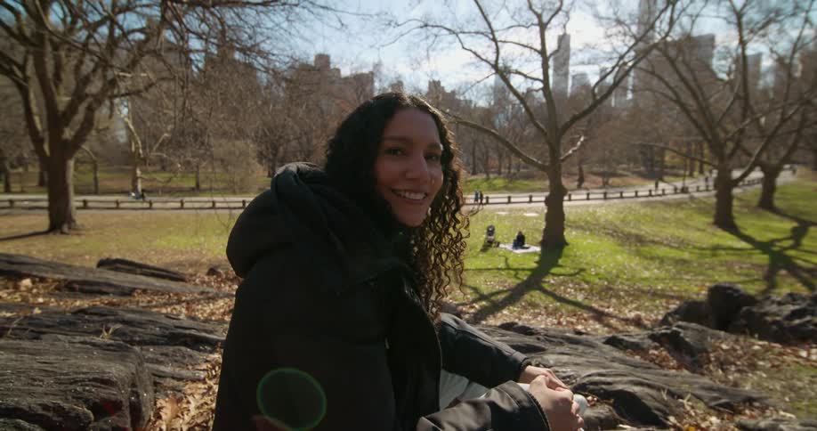 A woman smiles as she sits in a park in a large city