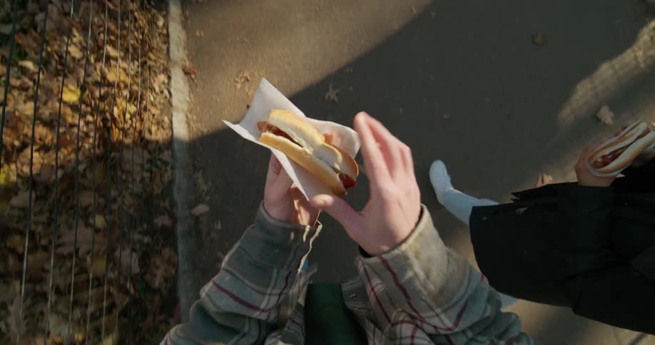 Two people are walking and eating hot dogs