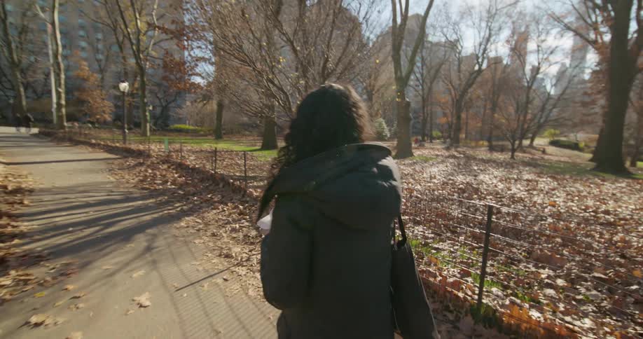 Following a woman walking in a park eating a hotdog while she looks back