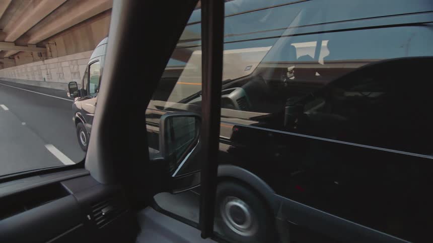 Interior passenger view of one black transport van passing another on the highway