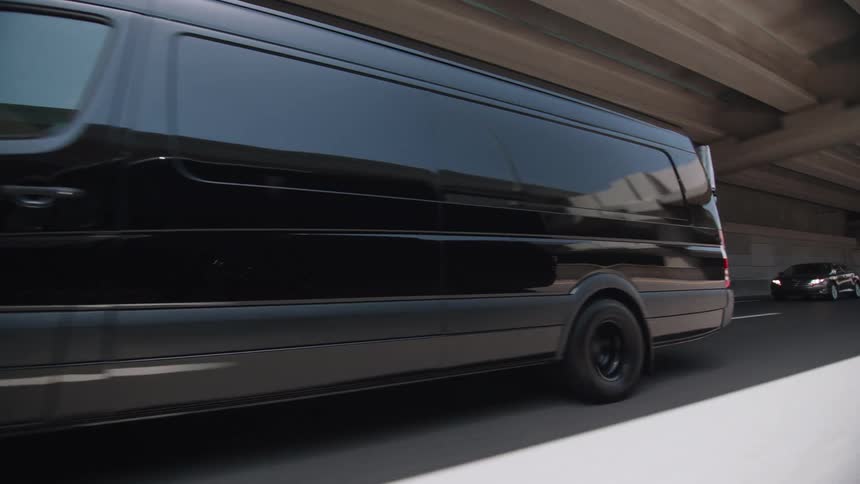 A large black van travels on highway on a bright sunny day