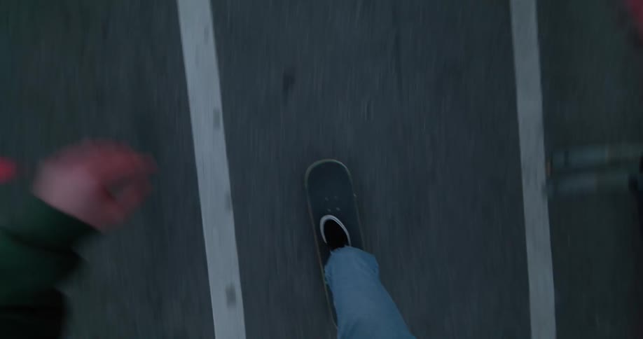A man drops his skateboard in the bike lane next to parked cars then pushes off
