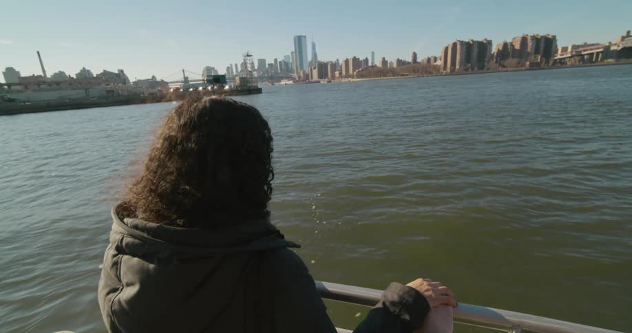 A woman looks over a boat railing on the river while holding hands with someone