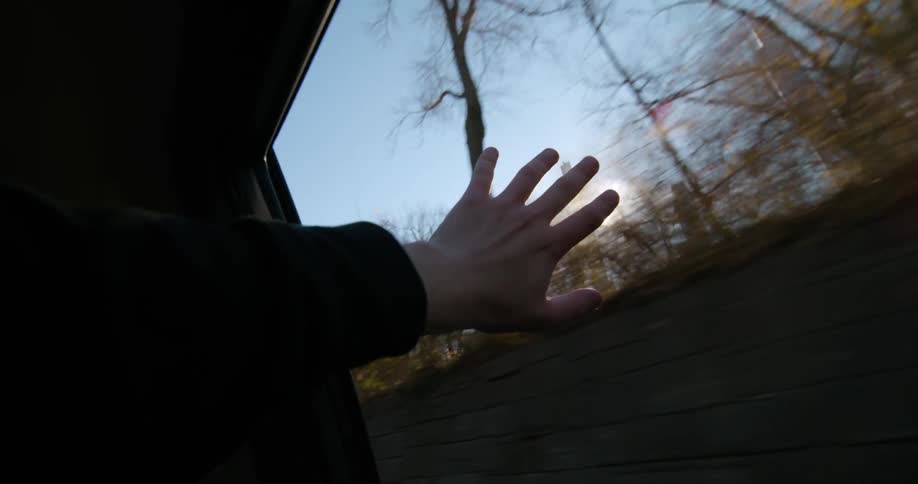 A person hanging their arm out the window of a moving vehicle with skyscrapers in the distance