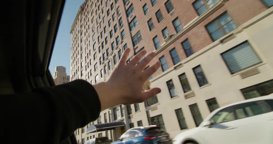 A hand reaches out of the back seat window pointing at the city buildings