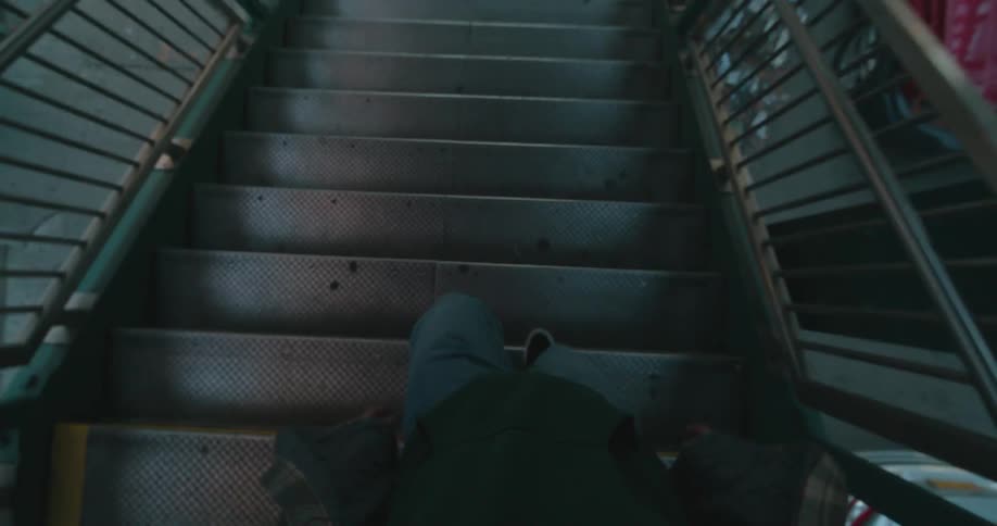 A man walks down the metal steps from a train platform to a city sidewalk