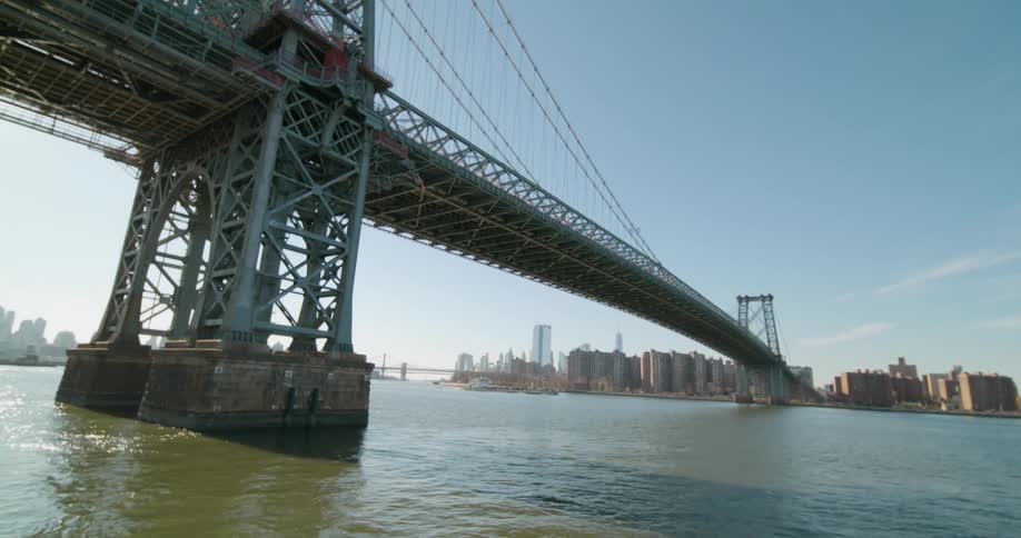 A woman walks to the railing and leans on it looking out at the bridge and city across the river
