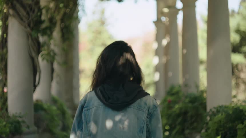 Woman walking down a path surrounded by pillars and plants