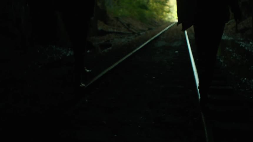 A man and a woman walk on some train tracks in a tunnel