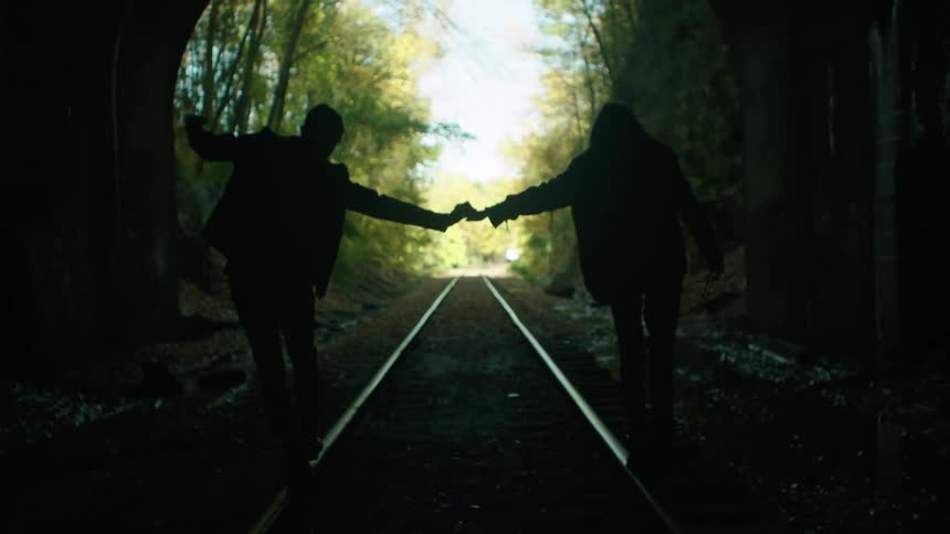 A man and woman hold hands and balance on a railroad track