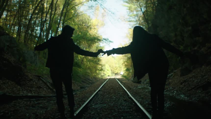 A man and woman hold hands and balance on a railroad track