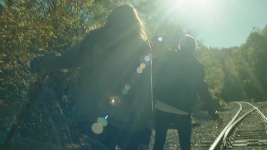 Two people are walking on a train track on a sunny day