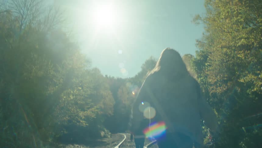 Two people walk on some train tracks in a rural area during the day