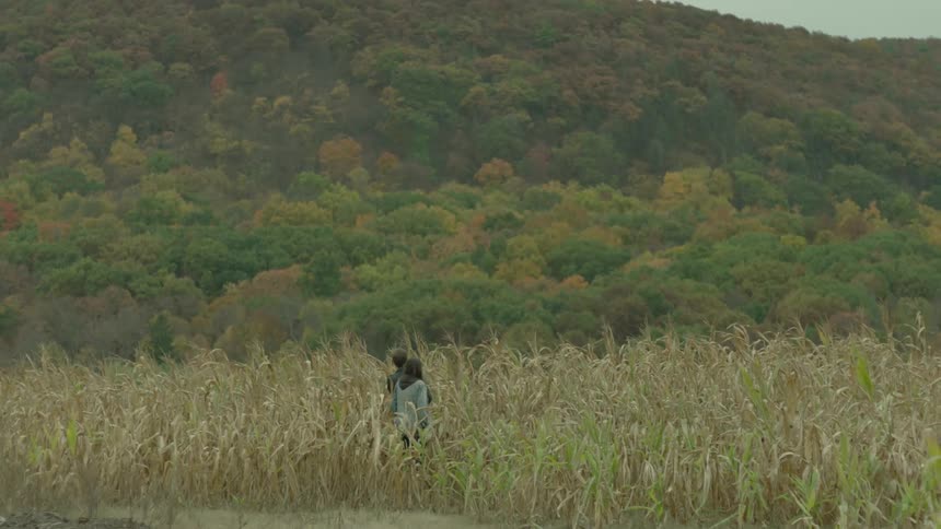 Two people hike amidst tall grasses in a hilly area