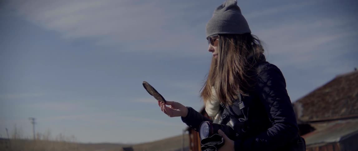 A woman picks up a round piece of metal from the sand