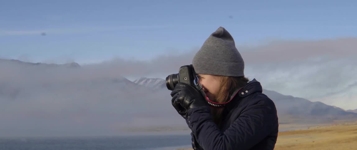 A woman is photographing near a cloud covered mountain