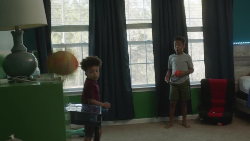 Two brothers play with balls staring shock as ball bounces off furniture near lamp