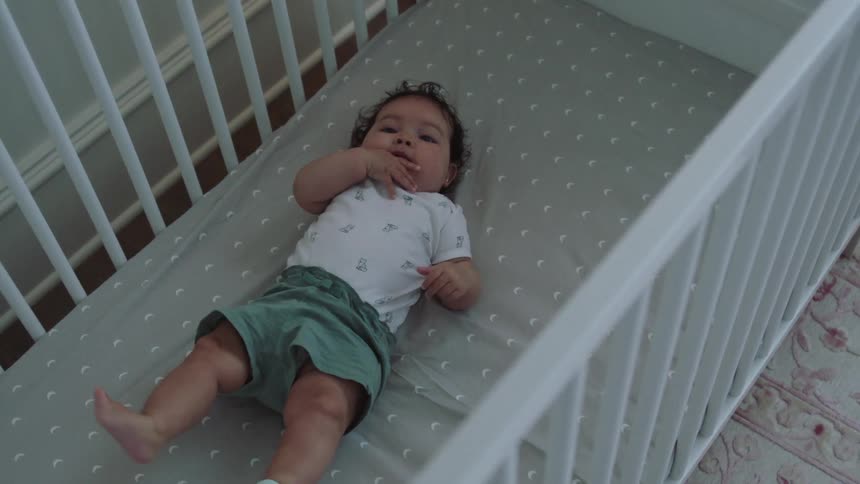 A baby girl lying in her crib kicking her legs happily