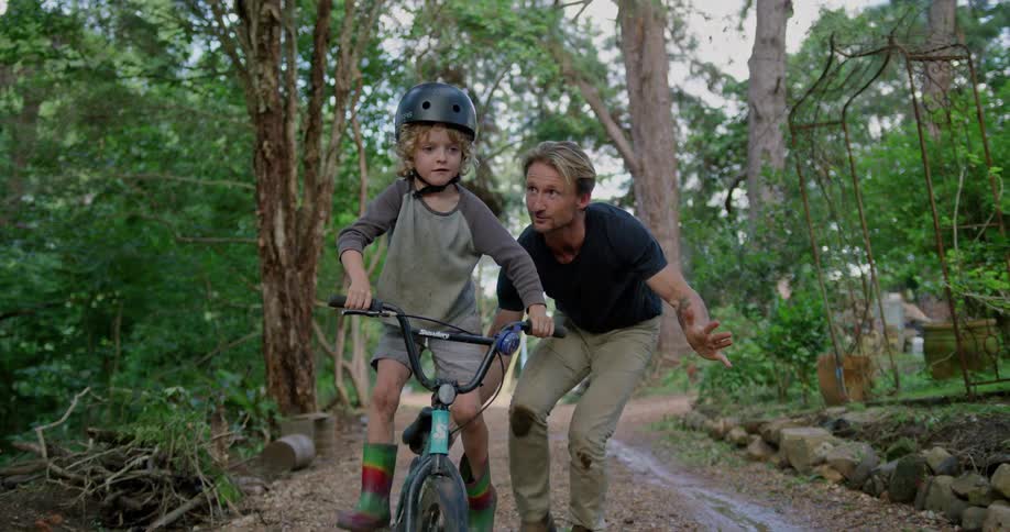Father celebrates as son rides bike down trail without training wheels