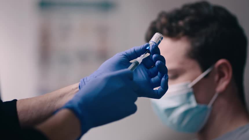 Young man watches as nurse prepares a syringe