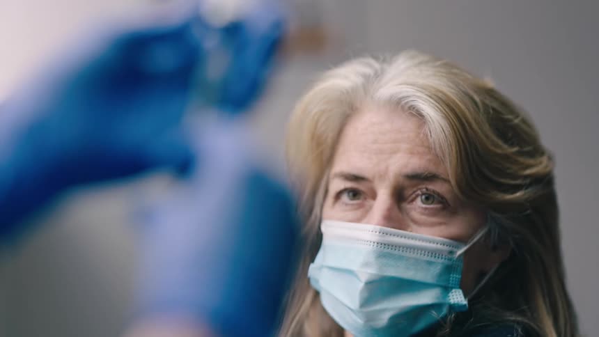 Patient sits in clinic and watches as a nurse uses a syringe to make her injection