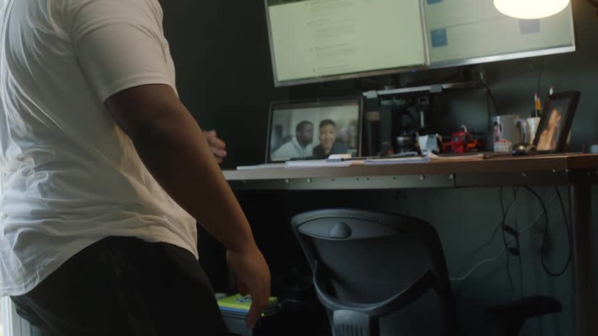 A man puts down his toddler son to work on his computer at a standing desk