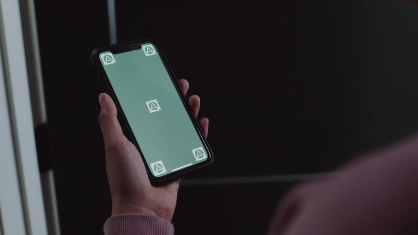 A person lifts their smartphone and swipes their phone across the screen indoors