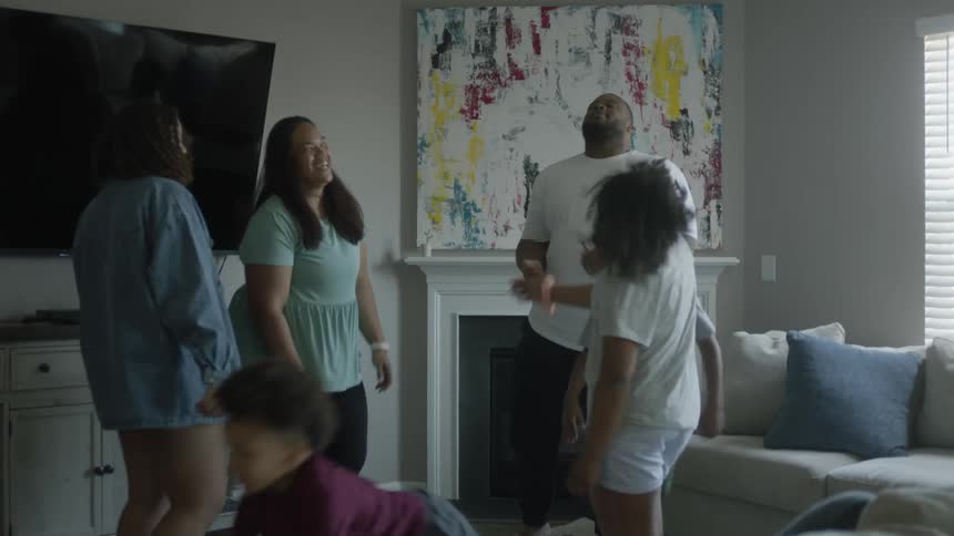 A family dances together in the living room of a house during the day
