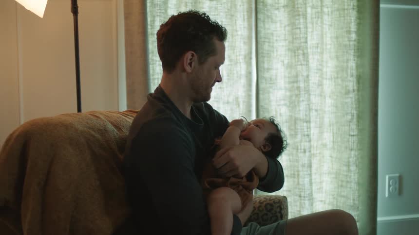 A father cradling an infant child while sitting in a chair at home