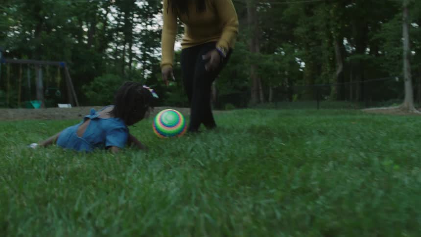 A little girl and her mother run in a yard playing with a ball
