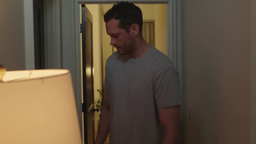 A depressed man walks through the corridor of a house before stopping and turning back