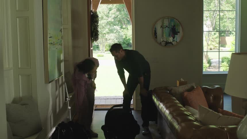 Family arrives at home from a vacation carrying a portable baby bed