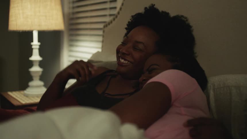Two women lay in bed laughing and talking