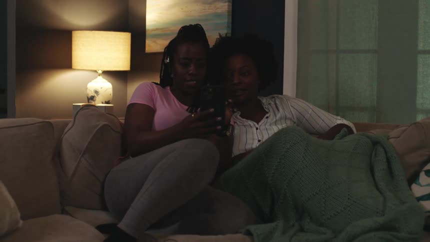 Two women sit on couch looking at mobile phone