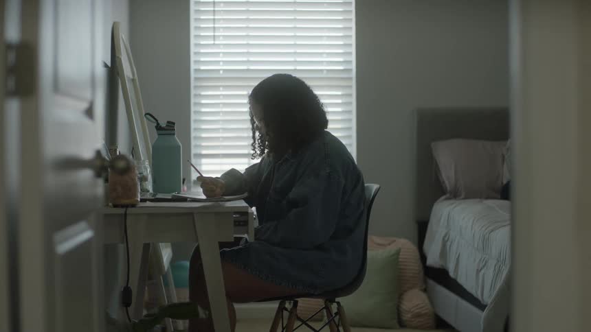 Young girl sitting at a desk in her bedroom doing homework with pen and paper
