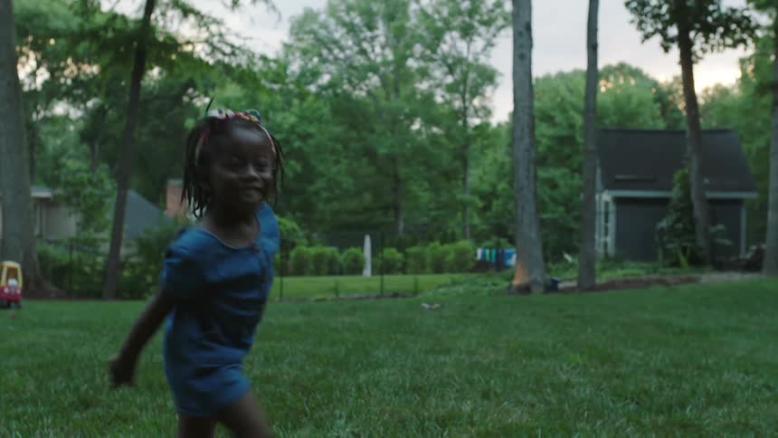 Black girl happily playing at her garden throwing a ball and laughing